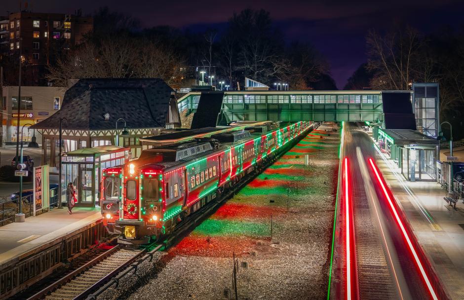 The M8 Holiday Lights Train waits for customers to board at Hartsdale Station while a northbound express to Southeast glides past on the opposite track, bringing a festive glow to an evening on the Harlem Line.