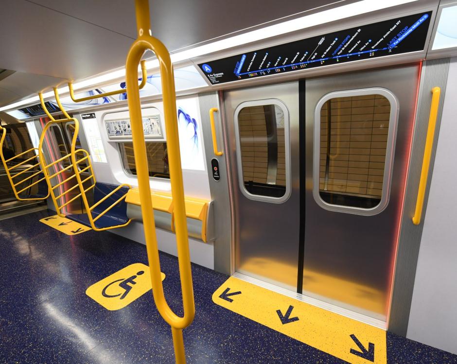 Accessibility features like a pole, fold-down seats, and digital signage inside a subway car.