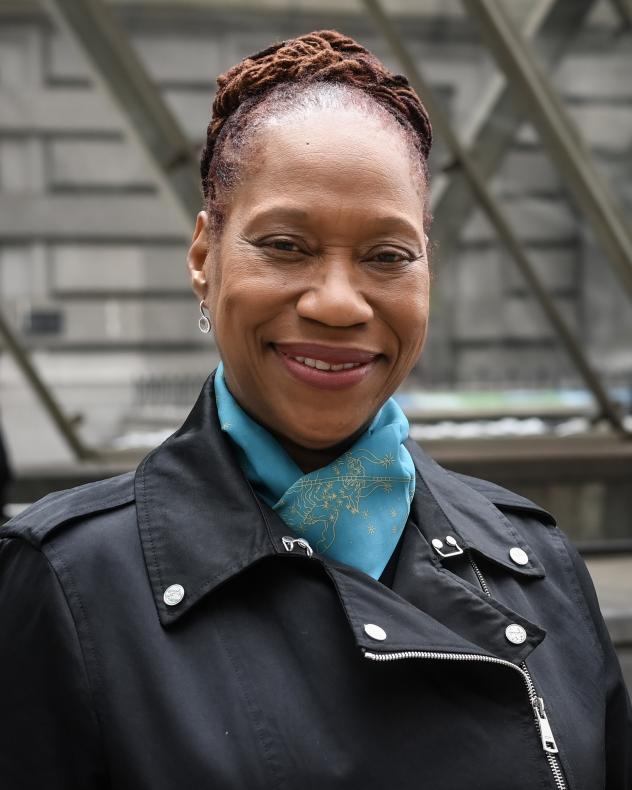 Anita Miller from the shoulders up wearing a dark coat and a green patterned scarf with the Bowling Green subway entrance in the background