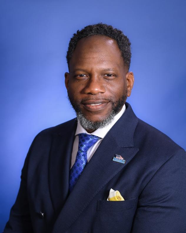 Christopher Leathers from the shoulders up wearing a dark blue suit, blue tie, white shirt, and SMART lapel pin