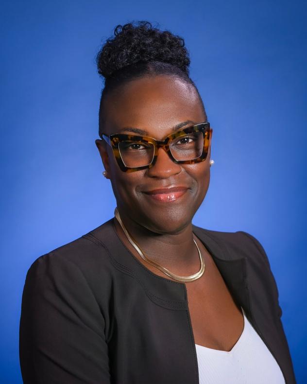 A photo of Melva M. Miller from the shoulders up wearing a dark jacket, white blouse, gold necklace, and horn-rimmed glasses