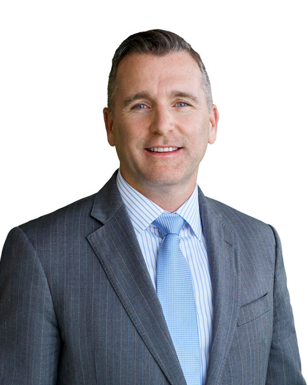 Photograph of a man wearing a gray suit and blue tie, smiling at the camera