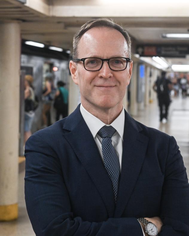 Photo of a man in a suit with glasses on a subway platform