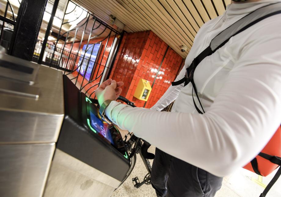 A woman uses a smart watch to pay the fare with an OMNY contactless reader at a subway turnstile.