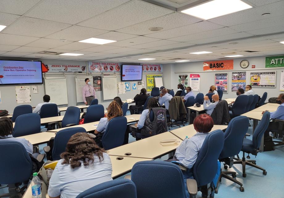 A group of people sit at desks in a room. 
