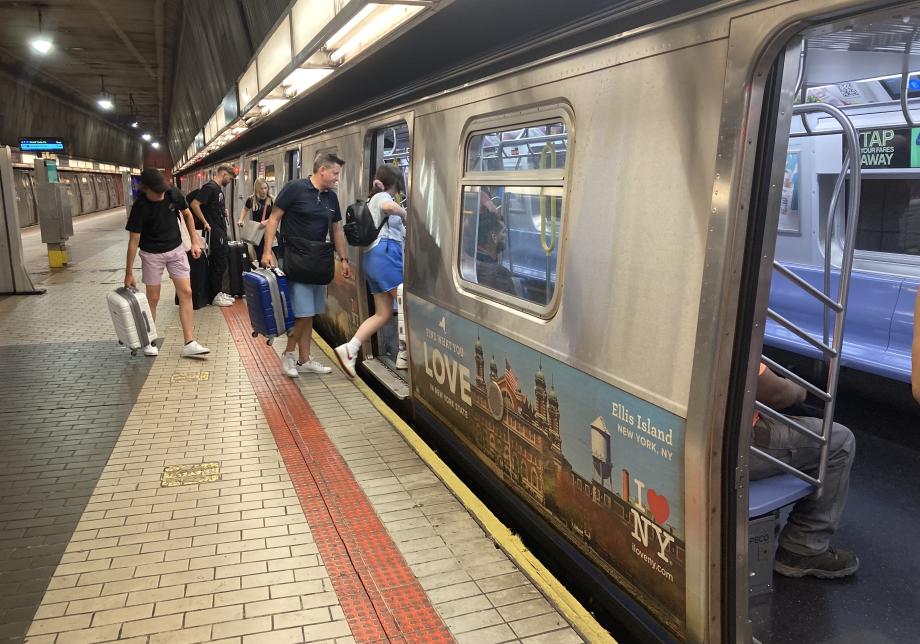 Passengers with luggage board the E train at Sutphin Blvd-JFK