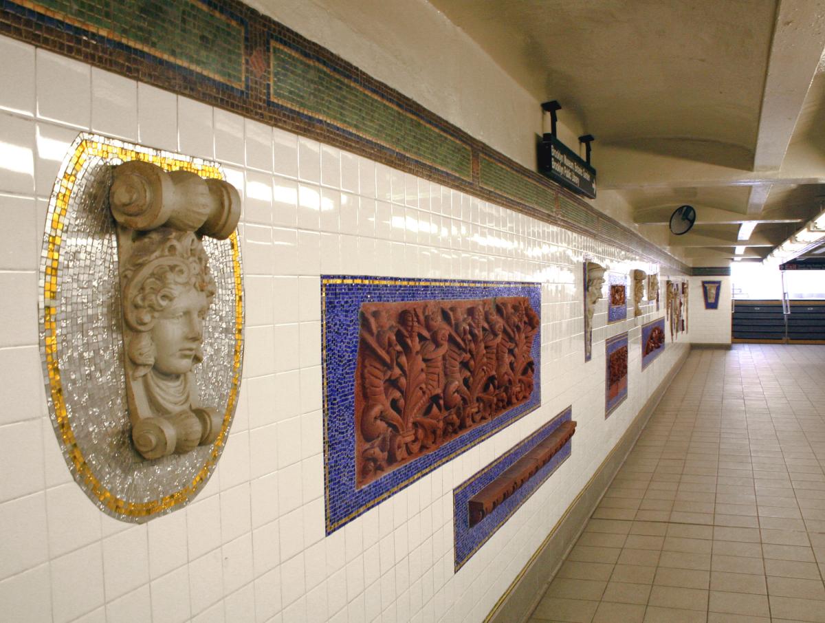 Artwork in terra cotta artifacts by the Arts for Transit Collaborative showing ornamental architectural forms salvaged from buildings and glass mosaic designs surrounding them on mezzanine and stairway walls. 
