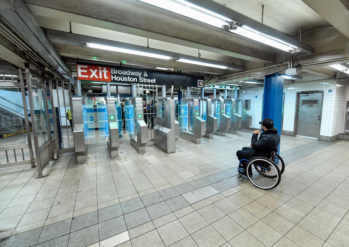 An array of modern fare gates with a wheelchair user viewing them