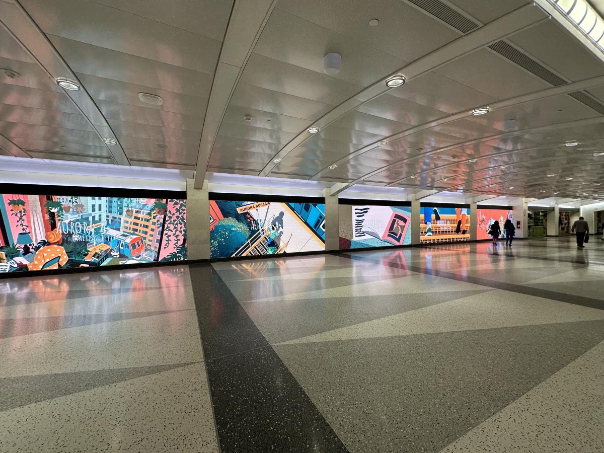 Large digital screens display colorful artwork along a corridor with people walking.