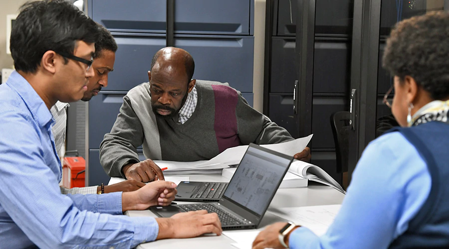 Four people sitting around a table looking at files and laptops. 