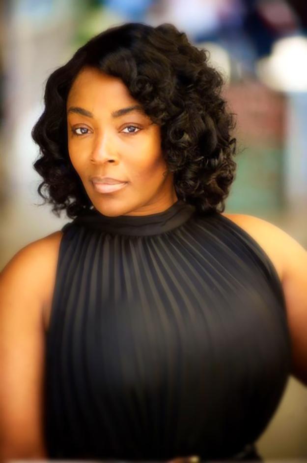 Woman in black dress posing in front of a blurred background.