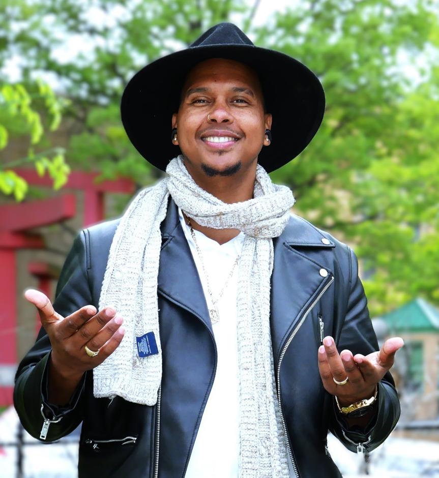Man in black leather jacket and black wide-brimmed hat in front of a tree.