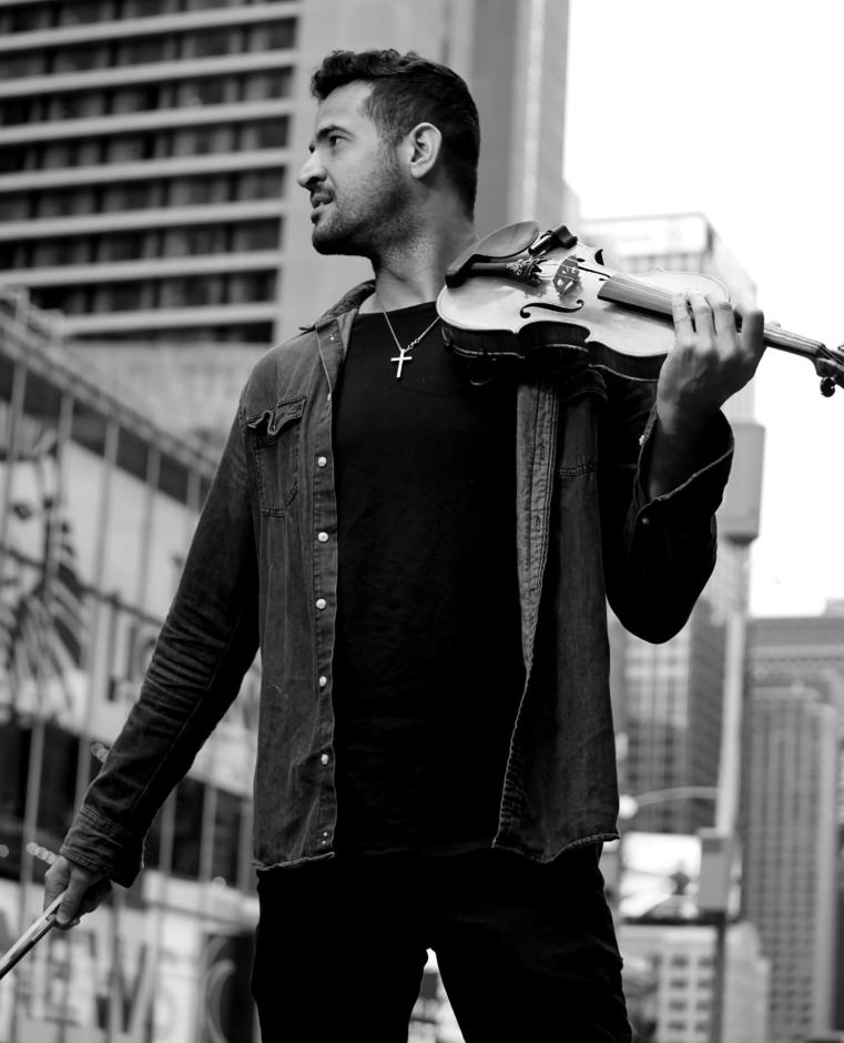Black and White photo of man in front of building window holding a violin.