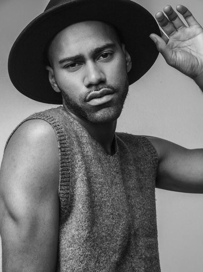 Black and White photo of man posing in a sweater vest and wide brimmed hat.