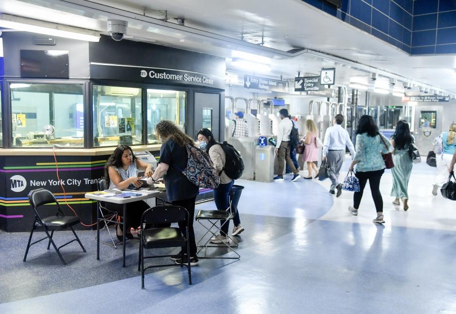 A Customer Service Center in a busy subway station, with a table outside where MTA representatives are talking to customers