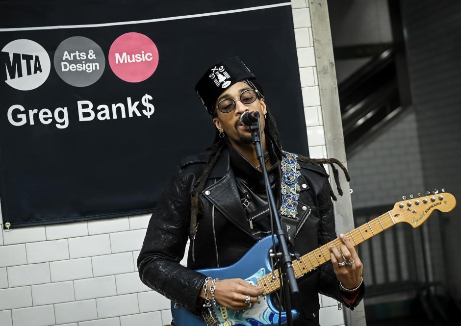 Musician performing with a guitar in front of a banner that says MTA Arts & Design Music.