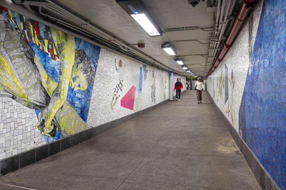 A long tunnel with vibrant mosaic art on white-tiled walls. 