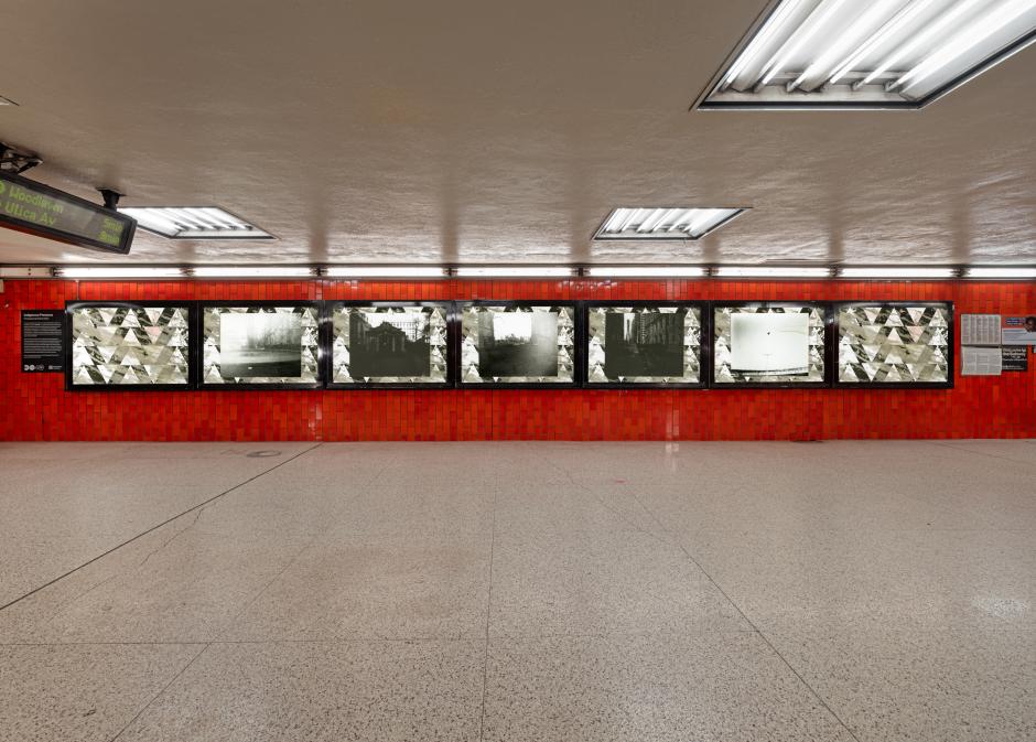 A subway station wall features six framed black-and-white photos, set against vivid red tiles.
