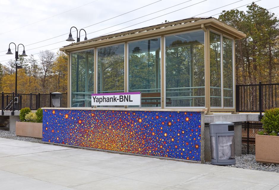 Glass shelter at the Yaphank-BNL train station with a bright, colorful mosaic on the platform wall.