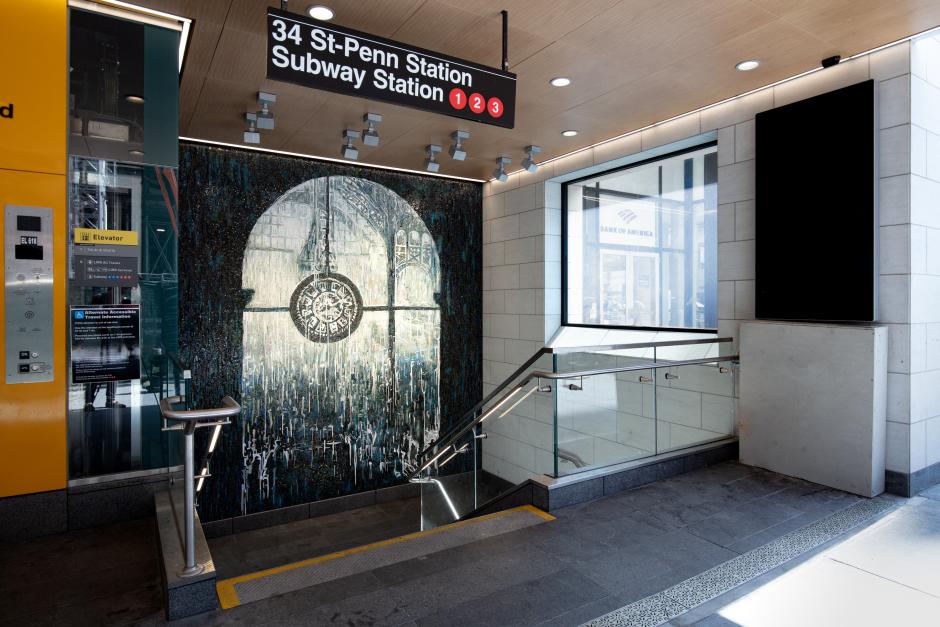 Mosaic artwork of a clock at 34 St-Penn Station, with a blue and silver backdrop, alongside signage for the station and an elevator.