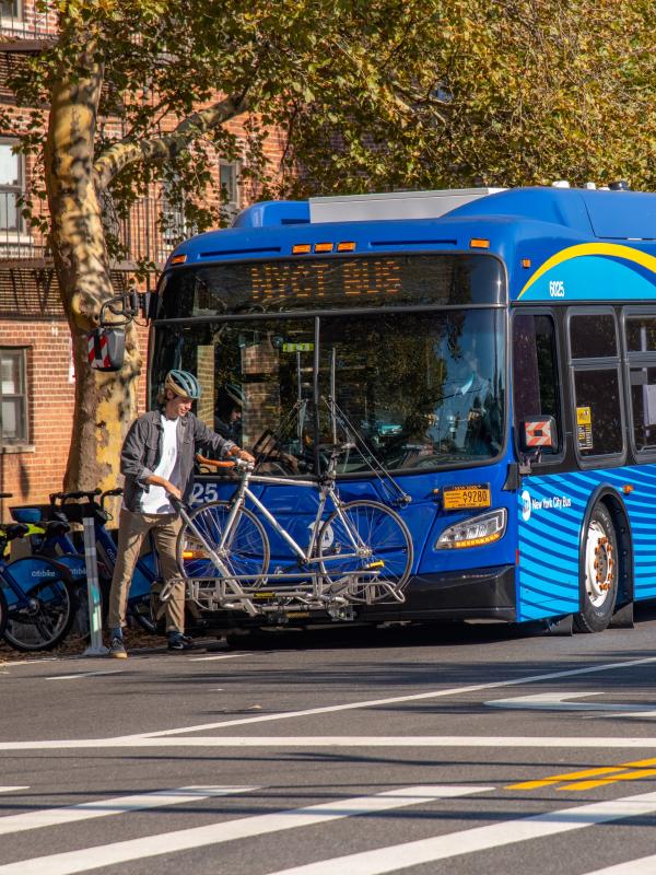 A person in a bike helmet securing their bicycle to a bus's bike rack