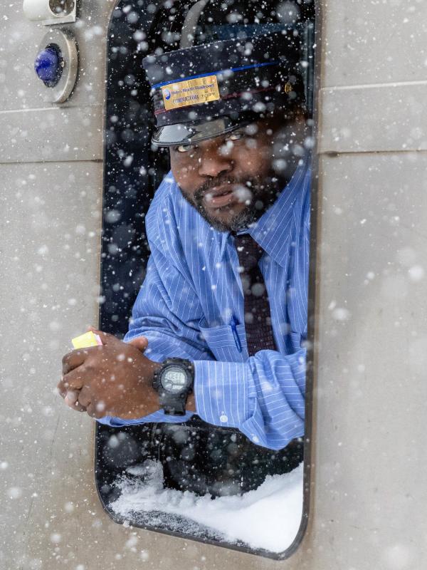 A railroad conductor leaning out the window of a train in the snow