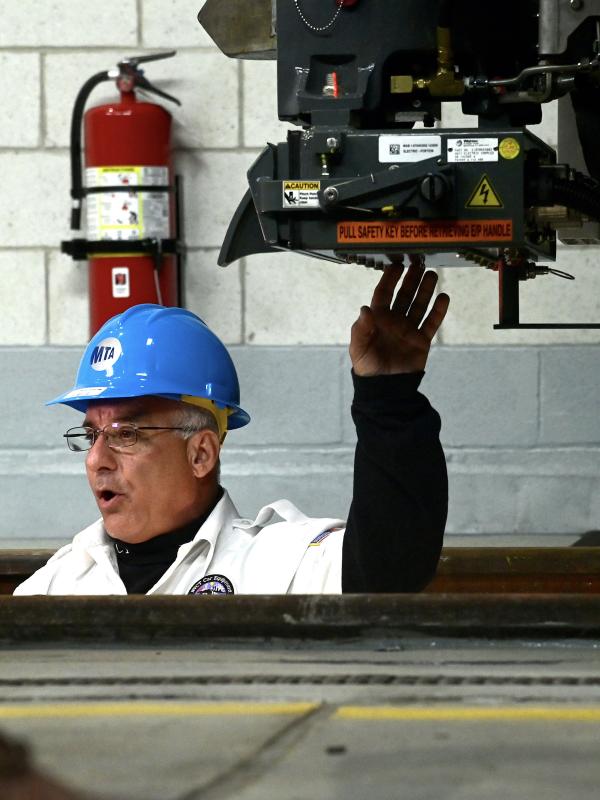 A car equipment employee in a white coat and hard hat standing in a pit underneath a train
