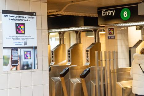 NaviLens promotional sign on a tiled wall. In the background, turnstiles and a sign that reads "entry 6." There is a NaviLens code on a column below the sign.